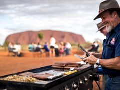 tour guide grilling sausages in uluru, sunset bbq
