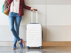 woman leaning against wall while holding luggage