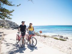 REX-Bike Hire-Couple walking with bikes next to beach_1920