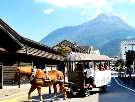 pixta95324917_由布院駅前の町並み・辻馬車の通る風景