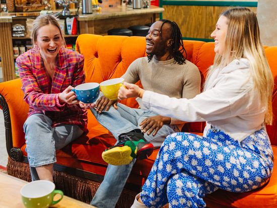 Three friends raising mugs on the couch at Central Perk, Landscape, TFE London